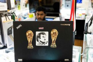 Ein Ladenbesitzer verwendet am 29. Oktober 2022 in einem Einkaufszentrum in Doha vor dem Fußballturnier der FIFA-Weltmeisterschaft Katar 2022 einen Laptop, der mit Bildern der FIFA-Weltmeisterschaftstrophäe und Katars Emir Scheich Tamim bin Hamad al-Thani (C) geschmückt ist. (Foto von Juwel SAMAD / AFP)
